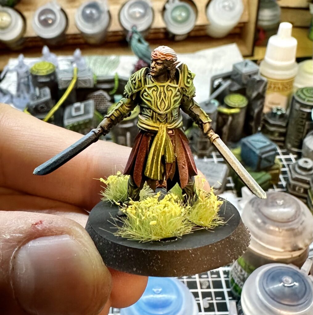 Painted elf noble miniature, wielding dual swords, standing in meadow flowers. He has an elaborate breastplate.