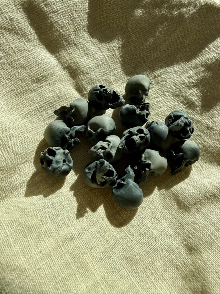 15 miniature skulls on a linen cloth. They're 3D printed resin models, painted dark fray.