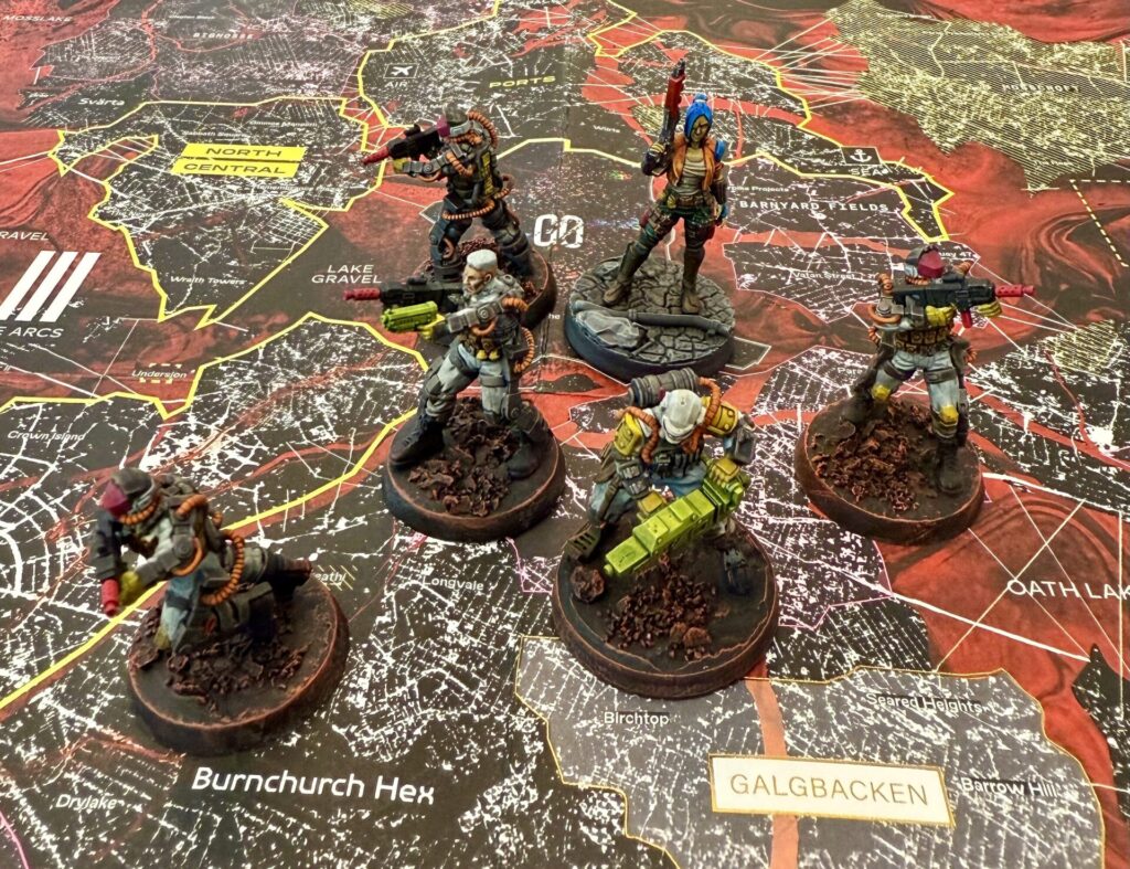 Painted miniatures on top of a map of the game's setting. The miniatures are grays and oranges, with bright details, going for an old comic book look.